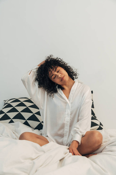 Young mixed race woman stretching neck in bed. Vertical image. Healthy lifestyle concept. - Fotografie, Obrázek