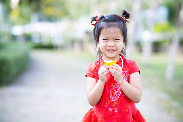 Sweet smile 4 year old kid girl wearing red cheongsam. Child holding gold ingot. Empty space to enter text. Happy Chinese New Year. - Valokuva, kuva