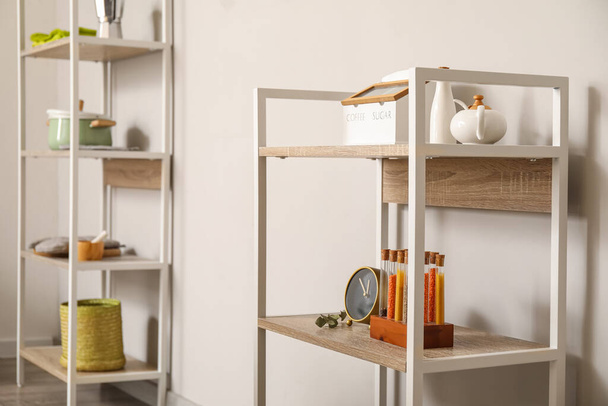 Shelving unit with teapot, spices and alarm clock near light wall - Foto, immagini
