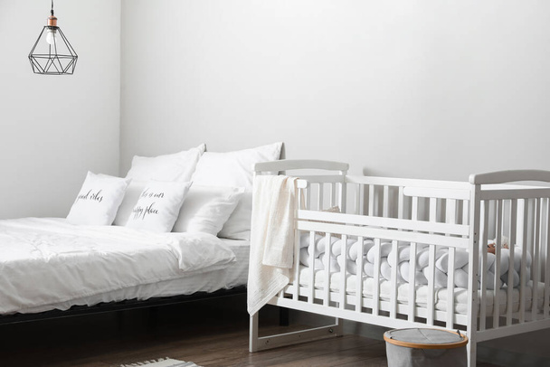 White crib and comfortable bed near light wall - Foto, Imagem