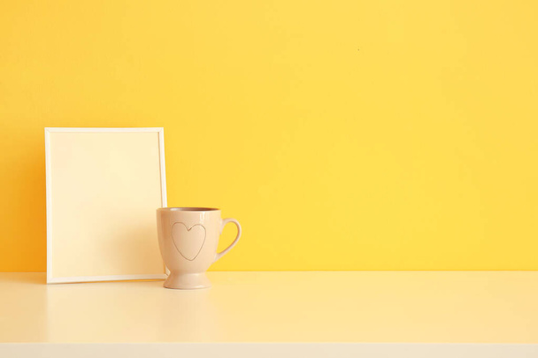 Blank photo frame and cup on table near color wall - Foto, immagini