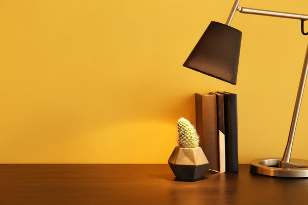 Glowing lamp, houseplant and stack of books on table near color wall - Foto, Imagem