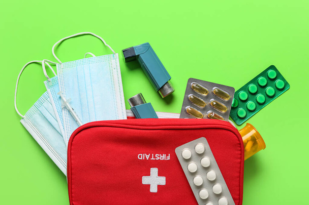 First aid kit with asthma inhalers, pills and masks on green background - Fotoğraf, Görsel