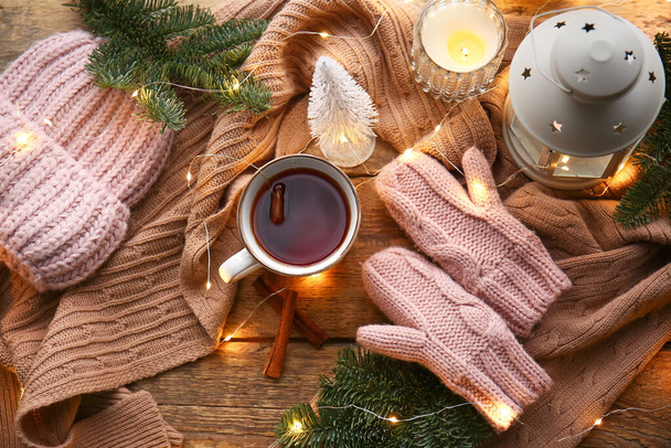 Warm gloves, scarf, hat, cup of tea and lantern on wooden background - Фото, изображение