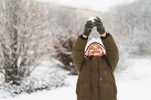 Cute little boy in funny winter hat walks during a snowfall. Outdoors winter activities for kids. - Photo, image