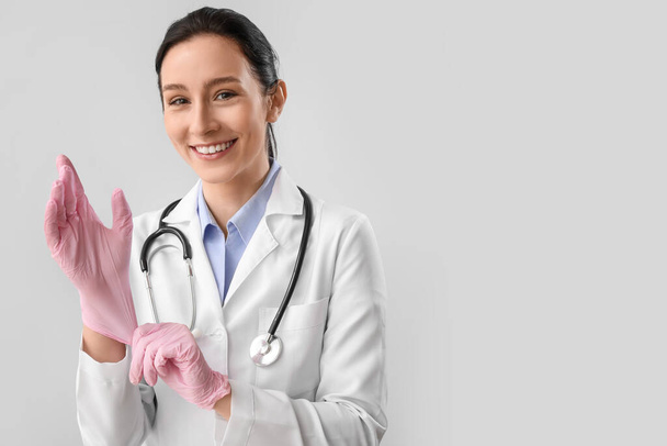 Portret van vrouwelijke arts zetten rubber handschoenen tegen grijze achtergrond - Foto, afbeelding