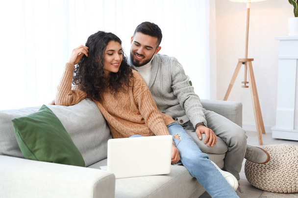 Heureux jeune couple avec ordinateur portable assis sur le canapé à la maison - Photo, image