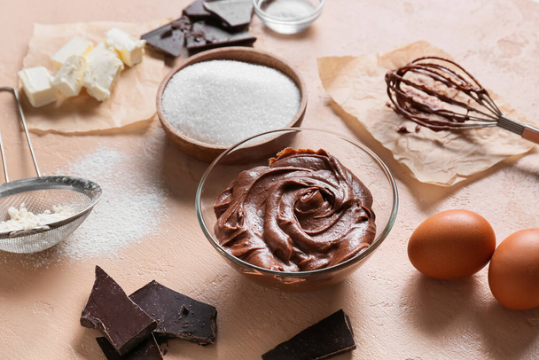 Bowl with fresh dough and ingredients for preparing chocolate brownie on beige background - Fotó, kép