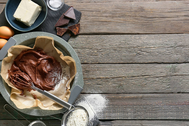 Tahta arka planda çikolatalı brownie hazırlamak için taze hamur ve malzeme içeren fırın tabağı. - Fotoğraf, Görsel