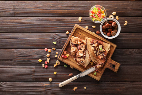 Panneau de crêpes fines savoureuses avec pâte de chocolat et noix sur fond de bois foncé - Photo, image