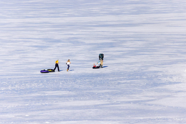 Eltern und zwei Kinder wandern in warmer Kleidung mit Schlitten und Ausrüstung zum Eisfischen über den zugefrorenen See - Foto, Bild