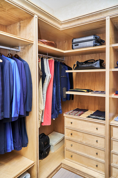 Stylish walk in closet with furniture of maple solid and veneer wood for clothes storage with crown molding in apartment - 写真・画像