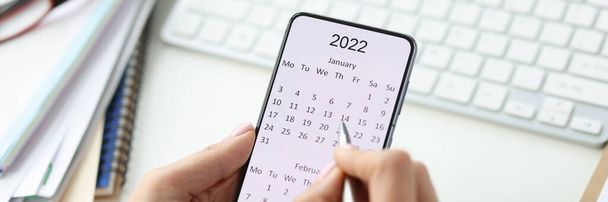Smartphone en pantalla con calendario para 2022 pluma en manos femeninas - Foto, Imagen
