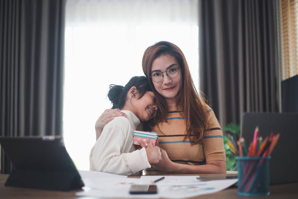 Happy Mother's day. Young woman mom getting congratulations from excited cute little daughter at home, child giving mother gift box while she working on laptop. Family holidays concept - Fotó, kép