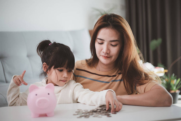 Matka a dcera dávají mince do prasátka. Rodinný rozpočet a koncepce úspor. Koncept juniorského spořicího účtu - Fotografie, Obrázek