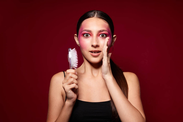 Mladá krásná žena s hřebenem v ruce světlé make-up představovat módní emoce růžové pozadí beze změny - Fotografie, Obrázek