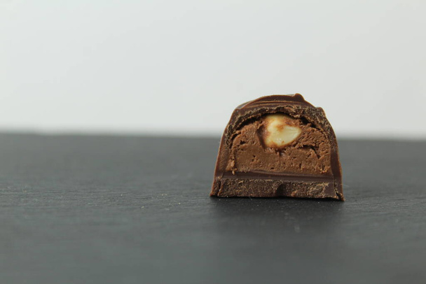 caramelo de chocolate con avellanas enteras de bosque de nueces con relleno de chocolate praliné en sección sobre un fondo negro oscuro con espacio para texto de copyspace. - Foto, imagen