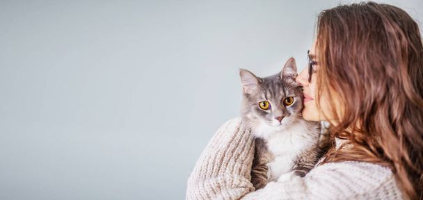 Young cheerful curly girl woman in glasses holding a beautiful gray fluffy cat in her arms - Photo, image