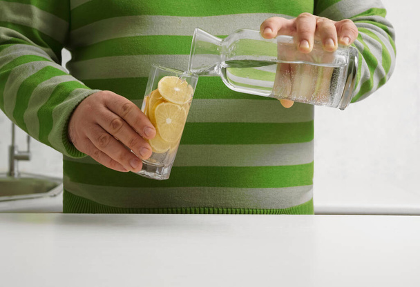 man pouring water from bottle to transparent glass  on background  kitchen interior. no face.  - Foto, Imagen