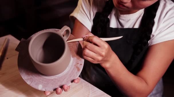Pottery in the art studio - woman holding a cup on the plate and smearing clay on the joint on the handle and a cup using a tool - Footage, Video