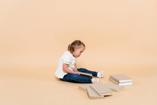 kid with down syndrome sitting near books on beige - Fotoğraf, Görsel