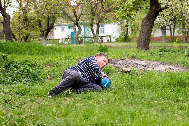 хлопчик на відкритому повітрі з м'ячем грає у футбол на траві у весняному селі
 - Фото, зображення
