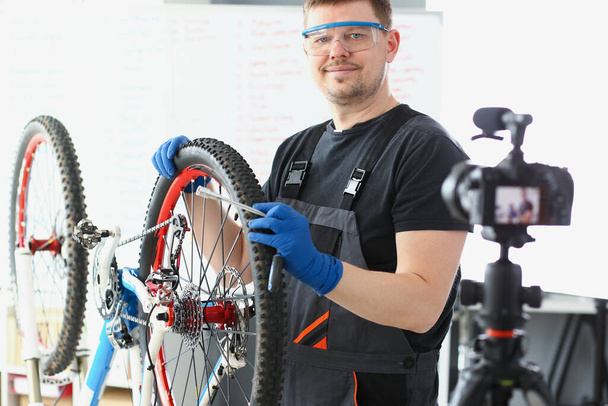 Qualified handyman fixing broken bicycle, filming process on videocamera - Fotó, kép
