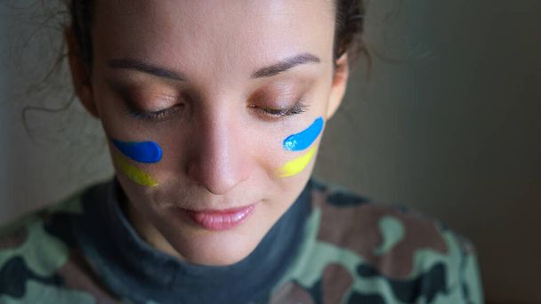Ritratto interno di giovane ragazza con bandiera ucraina blu e gialla sulla guancia indossando uniforme militare, coscrizione obbligatoria in Ucraina, concetti di uguaglianza - Foto, immagini