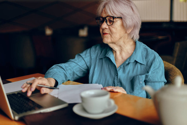Senior woman with glasses sits at a table in front of a laptop Lifestyle unaltered - Photo, image