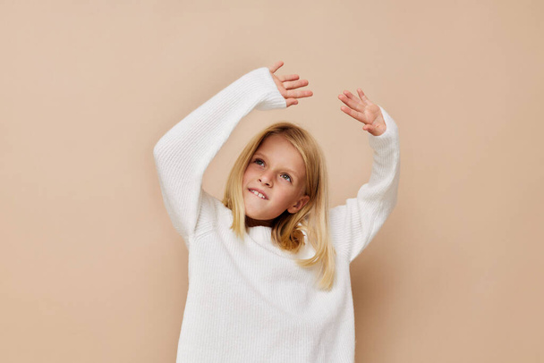 happy cute girl in a sweater, grimaces on a beige background - 写真・画像