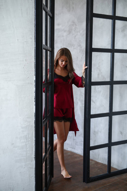 Beautiful young woman in red nightgown posing near black glass door - Foto, afbeelding