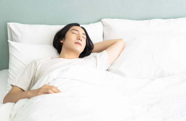 Portret van de jonge Aziatische man liggen ontspannen slapen in een gezellig wit bed en houden ogen dicht terwijl bedekt met deken in de ochtend. Guy genieten van zoete dromen, vredige tijd en energie te herstellen. - Foto, afbeelding
