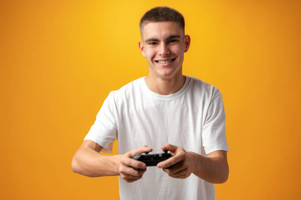 Young man playing computer games with jojystick against yellow background - Фото, зображення