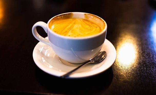 φλυτζάνι του cappuccino με κανέλα στο τραπέζι με ένα πιατάκι και κουταλάκι - Φωτογραφία, εικόνα