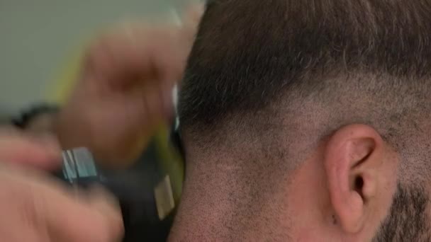 Ammattimainen parturi tekee hiustenleikkuun asiakkaalle käyttämällä sähkökonetta ja kampaa. - Materiaali, video