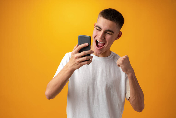 Joven adolescente hombre casual utilizando un teléfono inteligente contra el fondo amarillo - Foto, Imagen