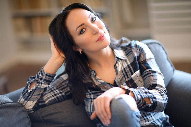 Portrait of young beautiful woman in plaid shirt reaxling at home - 写真・画像
