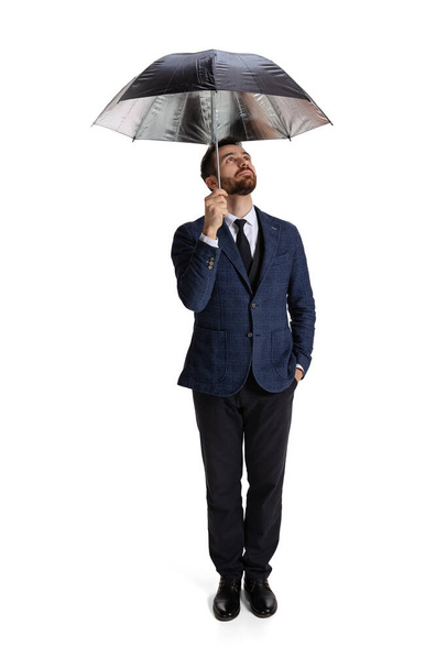 Full-length portrait of man in official suit, office worker standing under umbrella isolated over white background - Foto, Imagem
