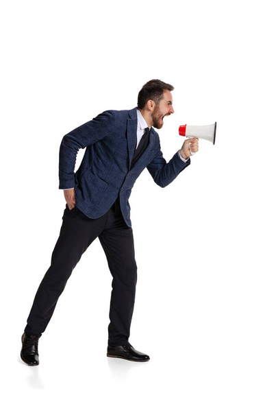 Full-length portrait of angry man, office worker shouting in megaphone isolated over white background - Fotó, kép