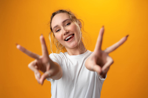 Portrait of a young funny woman showing peace gesture with two hands isolated over yellow background. - Fotografie, Obrázek