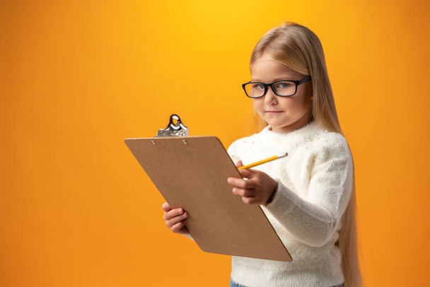 Portrait of little cute girl making notes against yellow background - Φωτογραφία, εικόνα
