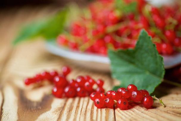 Red juicy currant lies on a wooden table and in plate. Fruits and berries. - Фото, зображення