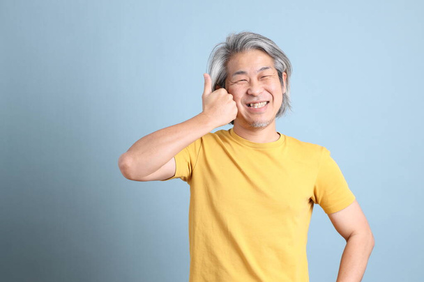 The senior Asian man with yellow t shirt standing on the blue background. - Photo, Image