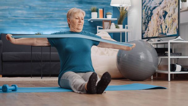 Senior persoon trekken weerstand band om te oefenen op yoga mat - Foto, afbeelding