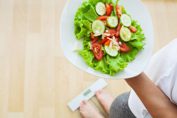 Γυναίκα μετρά το βάρος σε ηλεκτρονικές κλίμακες και σαλάτα δίαιτα - Φωτογραφία, εικόνα