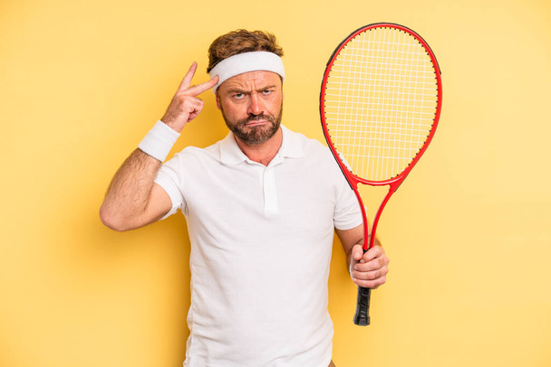middle age man feeling confused and puzzled, showing you are insane. tennis concept - Foto, immagini