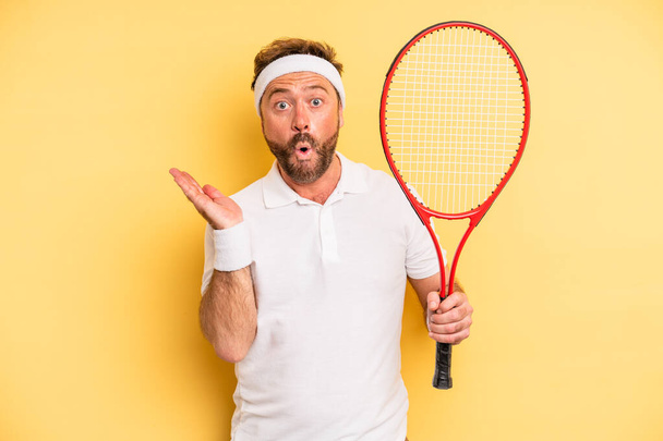 middle age man looking surprised and shocked, with jaw dropped holding an object. tennis concept - Zdjęcie, obraz