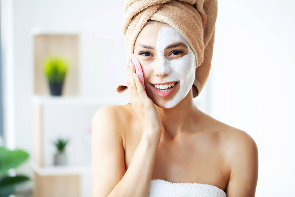 Beautiful young woman is getting facial clay mask at spa - Fotó, kép