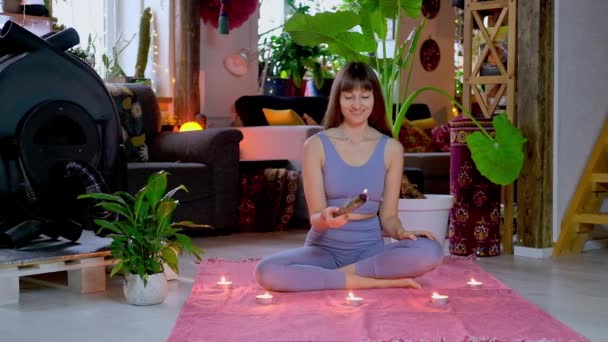 Woman sitting on floor, sets fire white sage incense for yoga meditation. - Filmati, video
