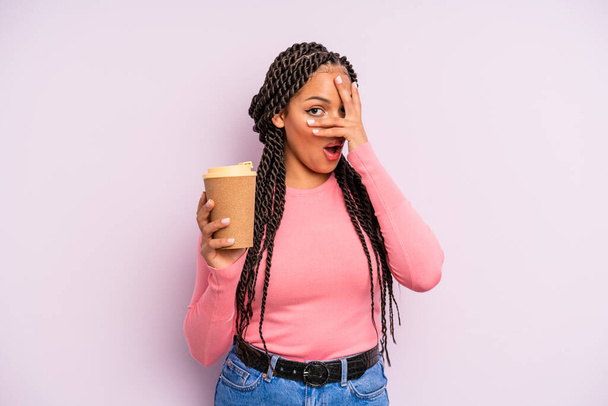 zwarte afro vrouw kijkt geschokt, bang of doodsbang, gezicht bedekkend met de hand. neem koffie mee - Foto, afbeelding